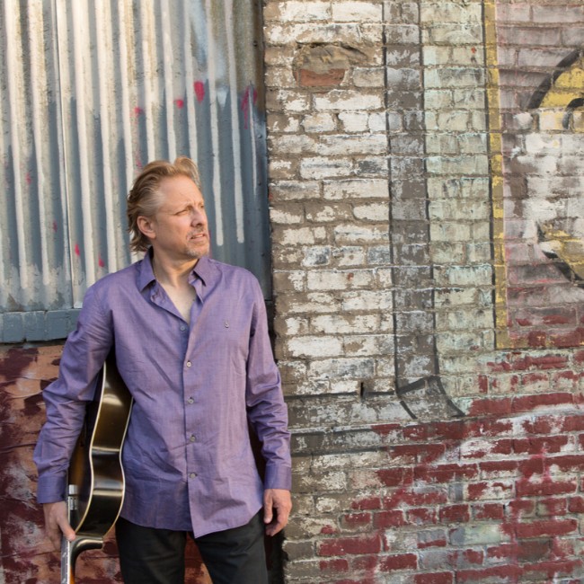 john bunzow holding guitar in front of graffiti wall