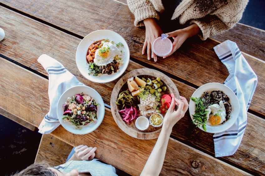 Two women's hands reaching over a table of food