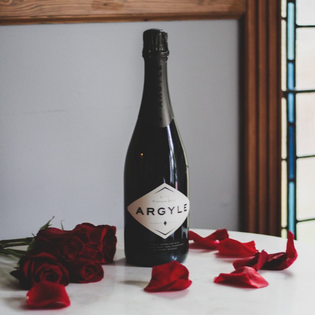 Bottle of champagne and red roses on white marble table